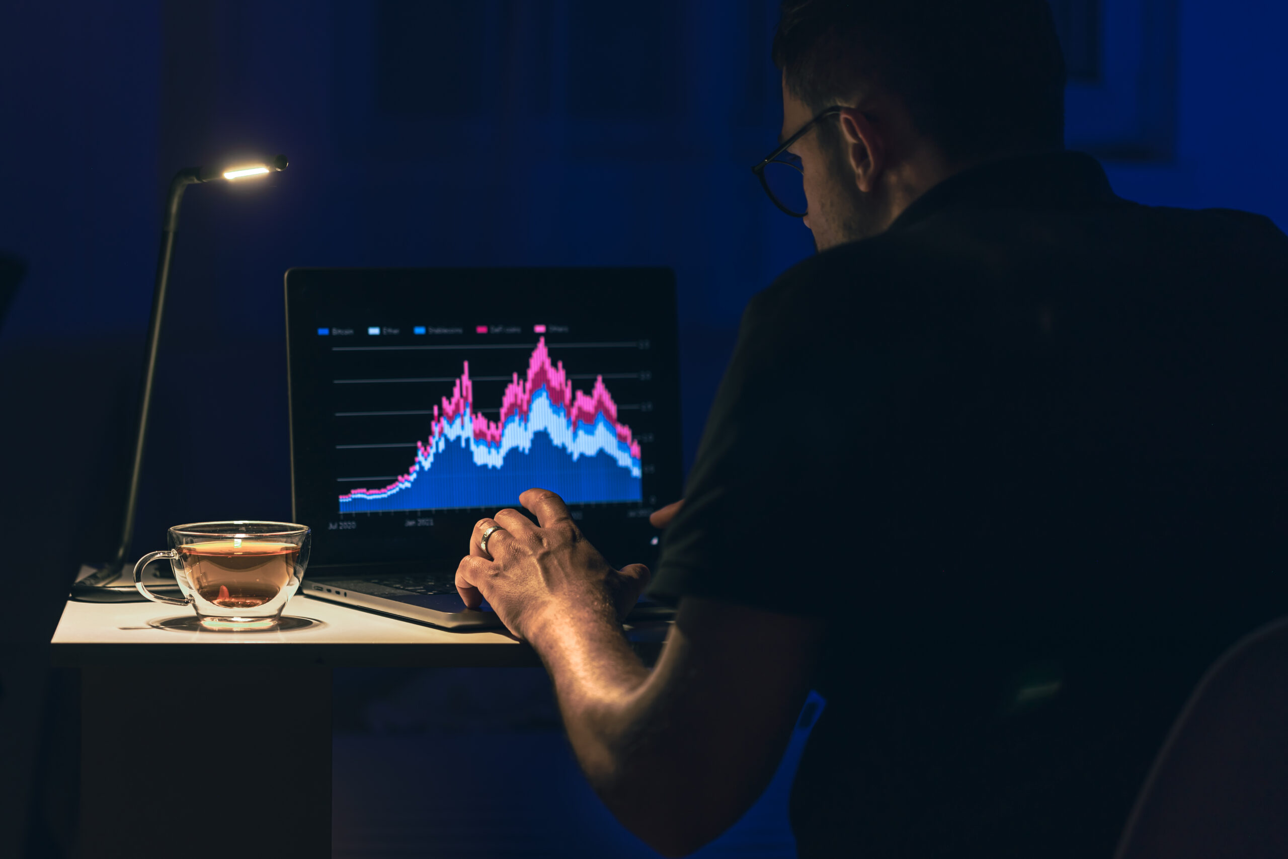Cómo Llegar a Ser un Trader: Guía Paso a Paso Man trading, browsing online stock investments at night. A man sits in front of a laptop with a chart. Business man stock exchange trader looking at laptop screen.